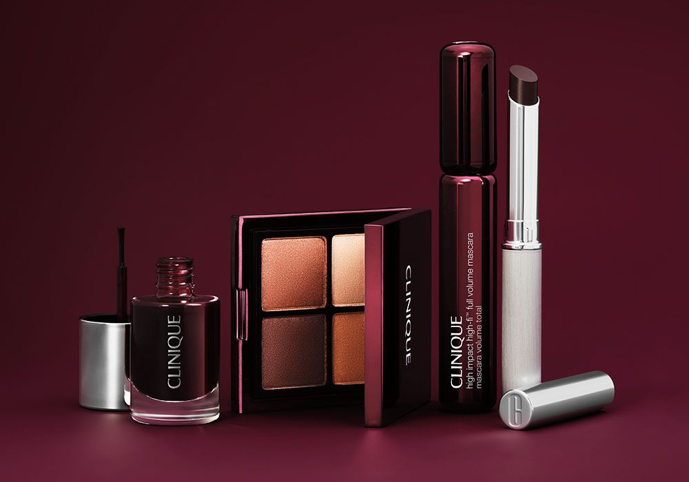 The Clinique Black Honey limited-edition collection displayed against a deep burgundy background, including the Color Rich Nail Polish, All About Shadow Quad in warm berry and bronze tones, High Impact High-Fi Full Volume Mascara and Almost Lipstick in Black Honey