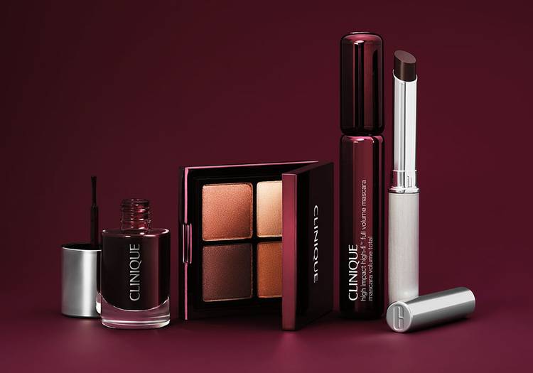 The Clinique Black Honey limited-edition collection displayed against a deep burgundy background, including the Color Rich Nail Polish, All About Shadow Quad in warm berry and bronze tones, High Impact High-Fi Full Volume Mascara and Almost Lipstick in Black Honey