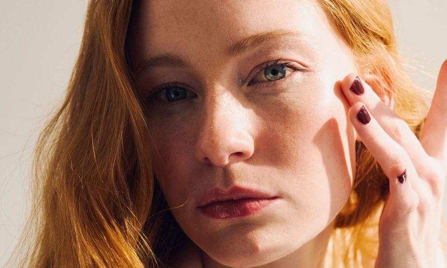 redheaded female touching her face softly with painted nails. Beauty and wellness concept