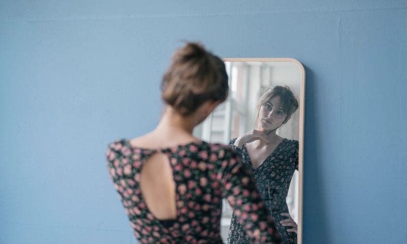 Young woman in vintage dress looking into mirror