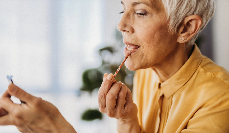 Mature woman applying lip color while looking in a mirror at home