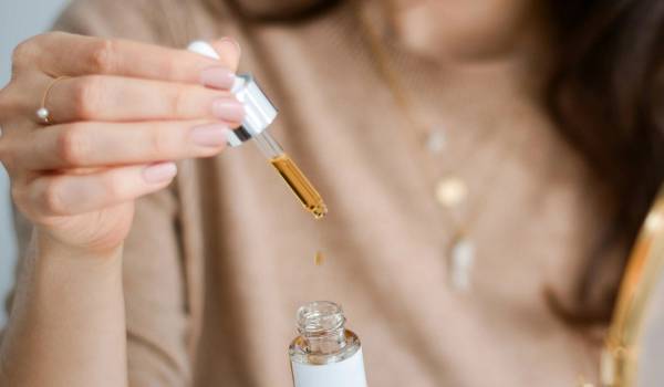 Close-up of a dropper releasing a drop of golden face serum into an open glass bottle, illustrating a fall hydration skin-care routine.