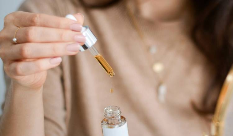 Close-up of a dropper releasing a drop of golden face serum into an open glass bottle, illustrating a fall hydration skin-care routine.
