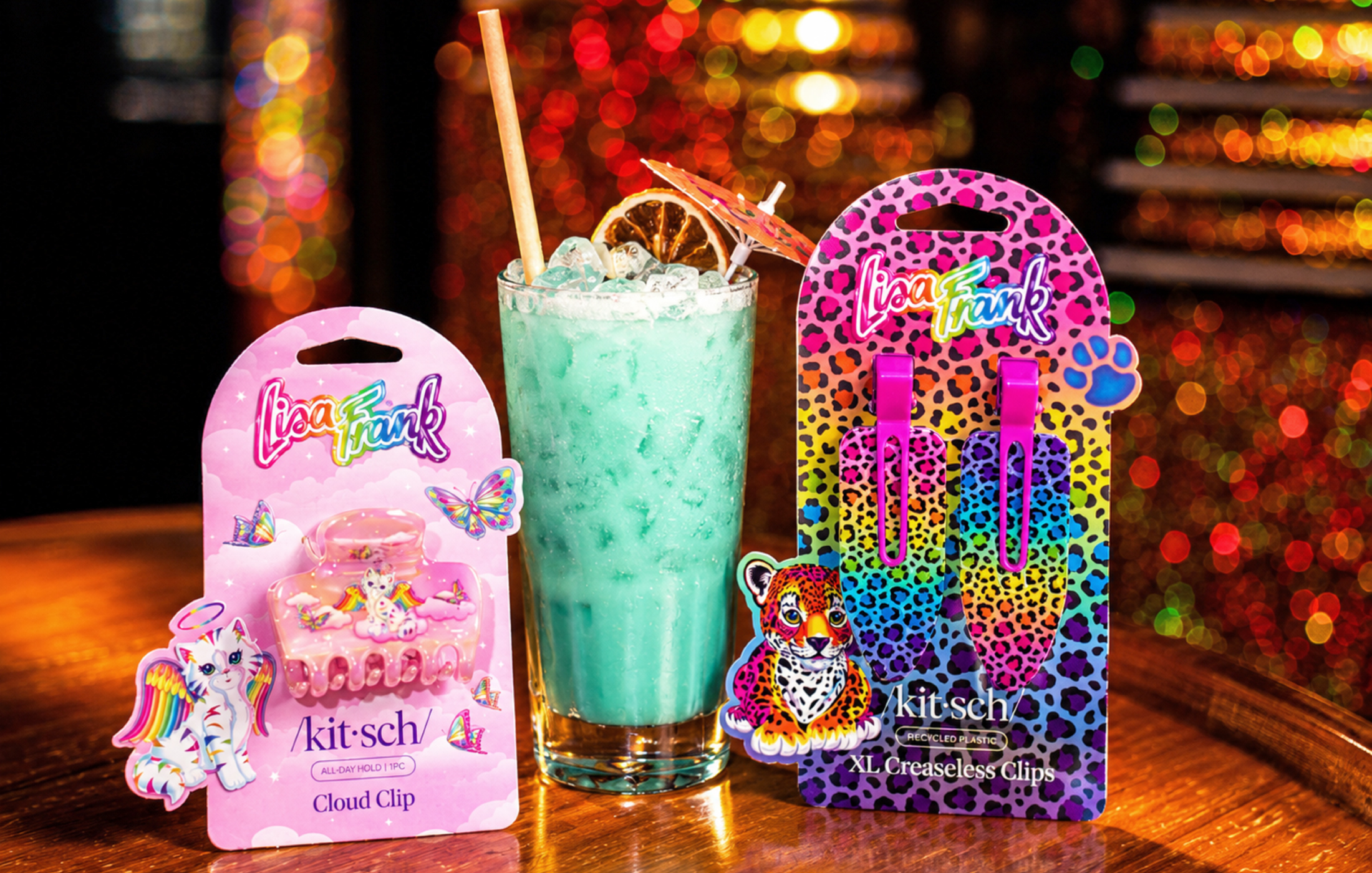 Kitsch x Lisa Frank hair clips flanking a teal cocktail with an orange slice and umbrella garnish at Broken Shaker