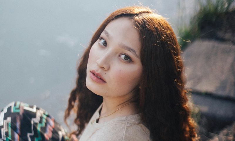woman in grey shirt sits on river bank