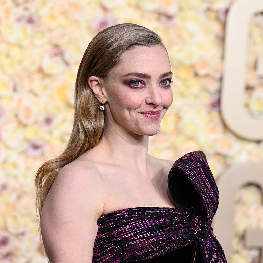 Amanda Seyfried posing on red carpet in a purple gown with soft wavy hair
