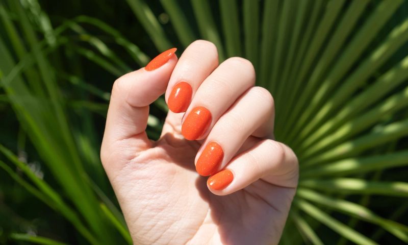orange nail polish on hand-with palm tree background