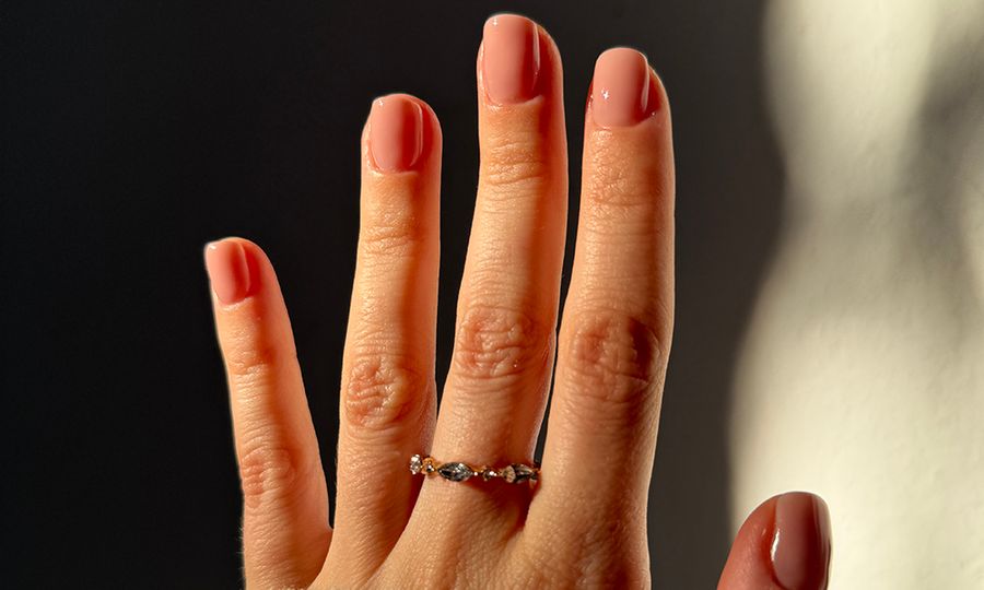Woman's hand with nude pink nail polish and golden ring, wearing a white sweater