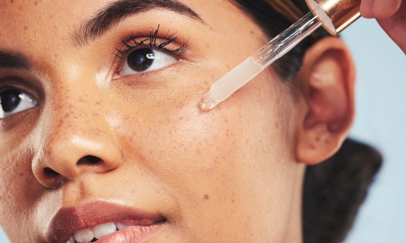 Woman, face oil and serum in studio for beauty of aesthetic skincare, dermatology and makeup on blue background. Closeup of model with dropper for facial cosmetics, hyaluronic acid and clean shine