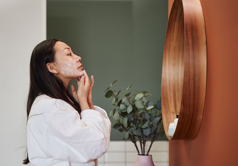 woman applying skin care in front of mirror