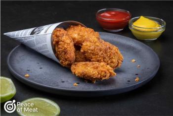 crispy plant-based chicken nuggets made from cultured chicken and plant-based protein. On plate in newspaper cone with ketchum, mustard, and lime on the side.