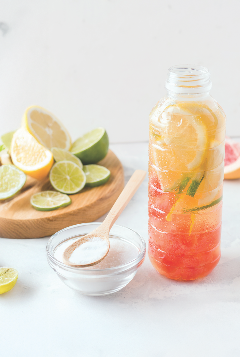water bottle with citrus fruit in it, next to bowl of white protein powder