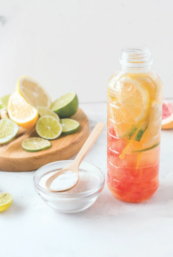 water bottle with citrus fruit in it, next to bowl of white protein powder