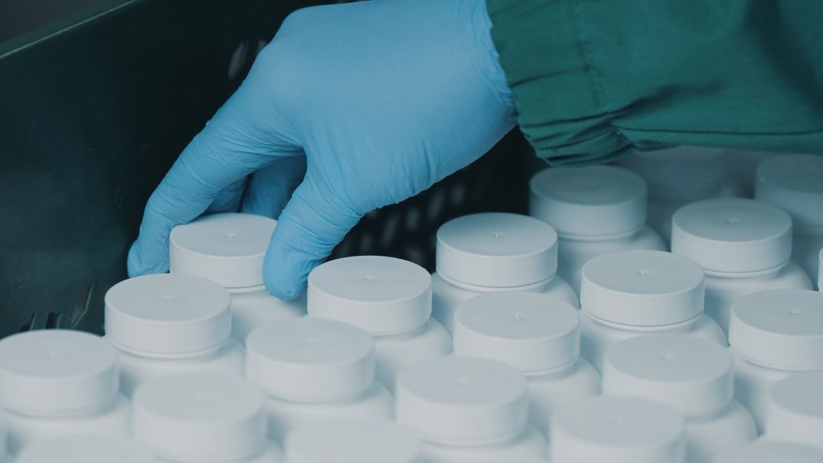 gloved hand grabbing dietary supplement bottle in manufacturing plant