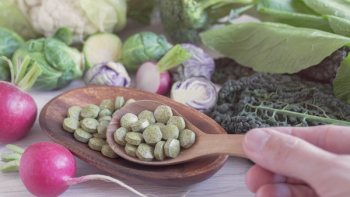green pills on wooden spoon and bowl surrounded by cruciferous vegetables