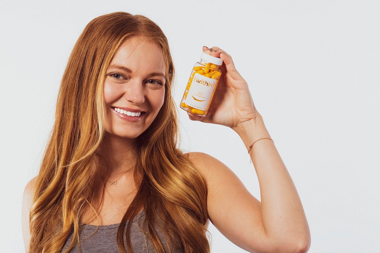 young woman with red hair smiling and hold up Clear Within supplement