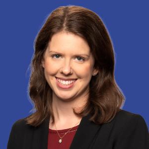 Headshot of a woman with shoulder-length brown hair wearing a black blazer with a maroon top