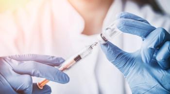 Image of a vaccine being prepared by a person in a white coat and blue gloves