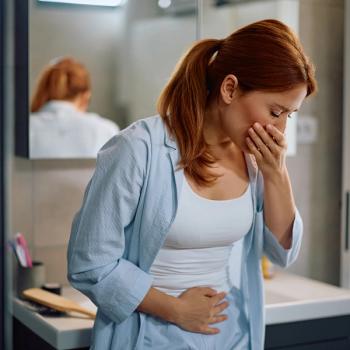 Photo of a person in a bathroom holding their abdomen and mouth