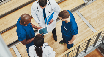 Aerial photo of four medical professionals talking in a huddle; two are wearing scrubs and two are wearing lab coats