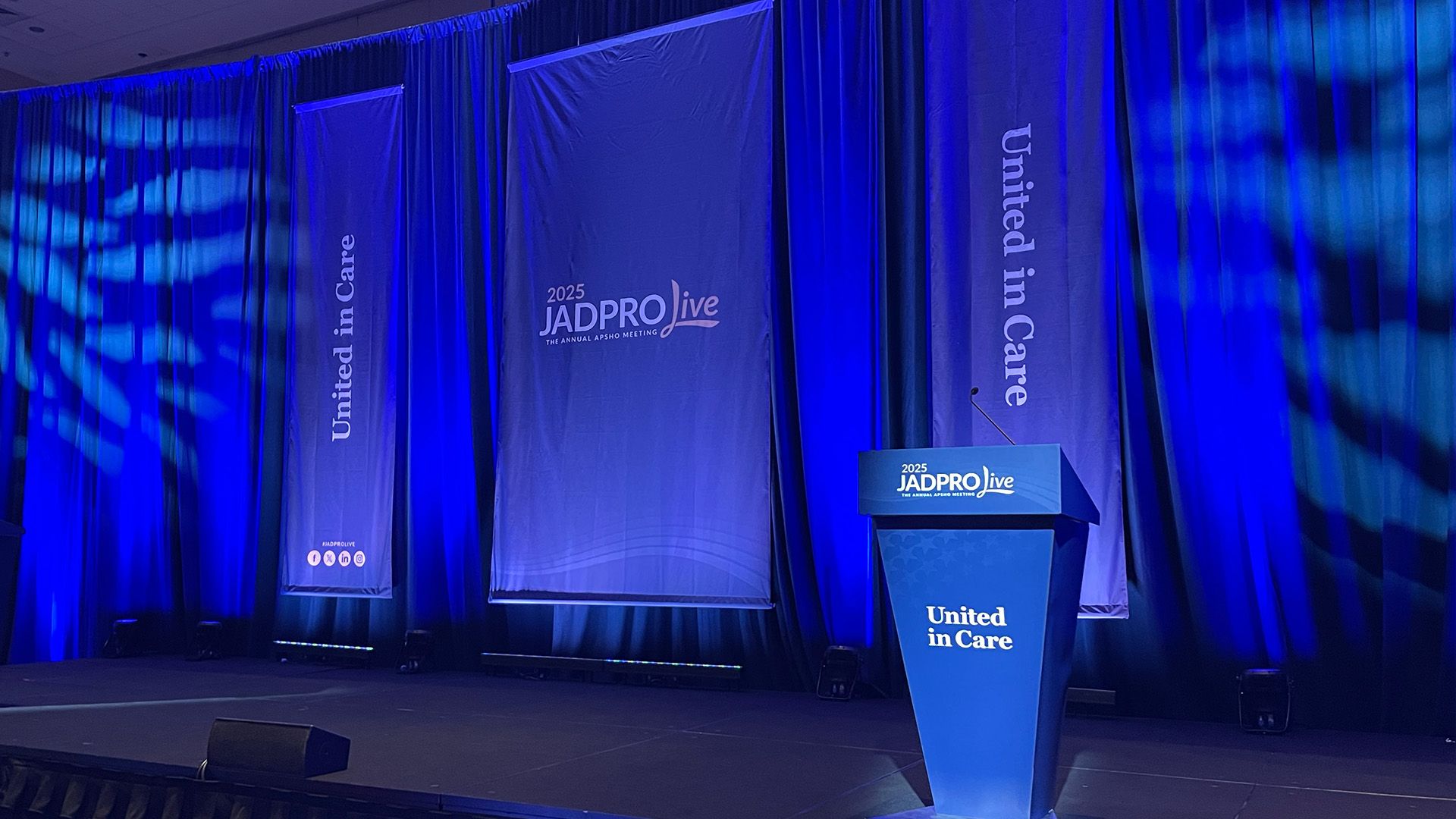 Image of a stage with banners and a podium that say "JADPRO Live"