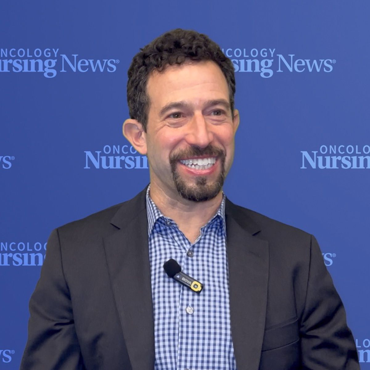 Photo of a white man with curly hair and in front of a blue Oncology Nursing News backdrop