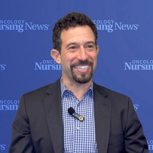 Photo of a white man with curly hair and in front of a blue Oncology Nursing News backdrop