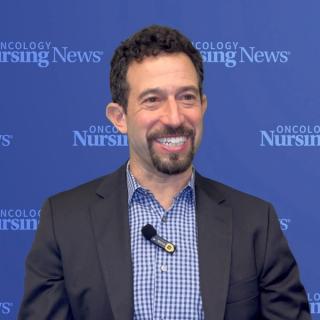 Photo of a white man with curly hair and in front of a blue Oncology Nursing News backdrop