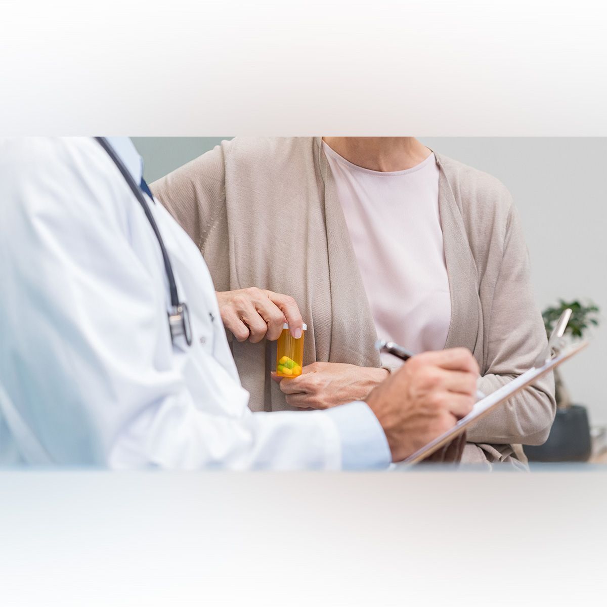 Photo of a patient holding a prescription bottle of pills and speaking with a doctor holding a clipboard