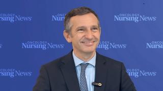 Photo of a man wearing a suit in front of an Oncology Nursing News backdrop