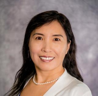 Headshot of a woman with black hair wearing a pearl necklace and a white blouse