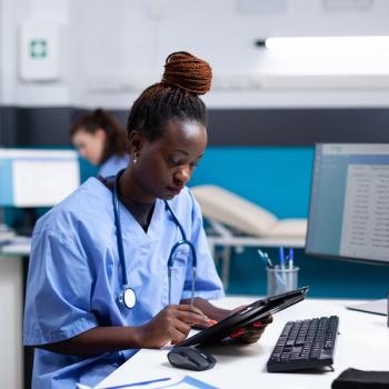 Photo of a nurse recording data on a computer and tablet