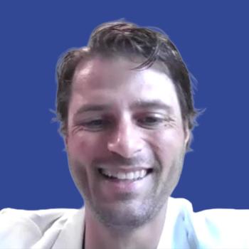 Photo of a man with brown hair smiling in front of a dark blue background