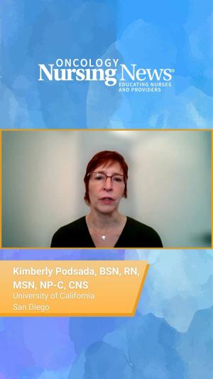 Photo of a woman with red hair and glasses wearing a black blouse and cross necklace in front of a dark blue background