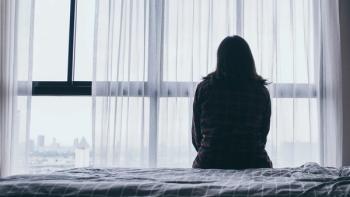 image of a person in shadow sitting on a bed and looking out a window