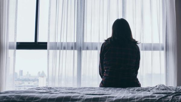 image of a person in shadow sitting on a bed and looking out a window