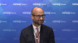 Man in suit standing in front of blue watercolor Oncology Nursing News backdrop