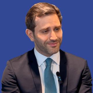 Photo of a man wearing a suit with a blue tie in front of a dark blue background