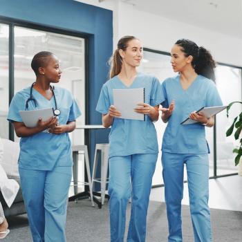 Photo of 3 people wearing scrubs talking in a hallway