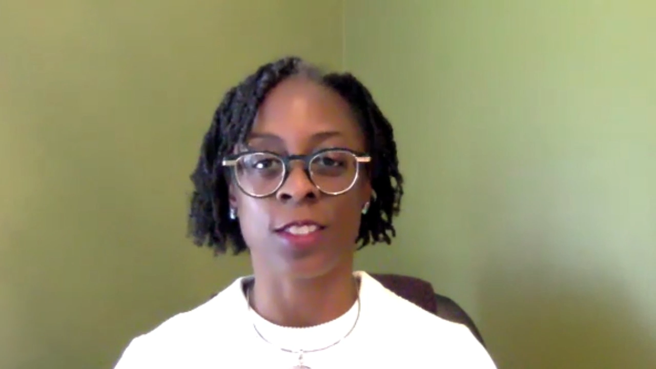 a woman with a white shirt and glasses sitting in front of a green wall.