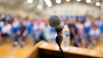 A microphone is in focus on a lectern or podium. Behind it, out of focus, is an audience. Concept image for named award lectures during the 2025 American Academy of Ophthalmology meeting. Image credit: ©Kathy images – stock.adobe.com