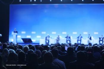 An auditorium full of people in a lecture hall, paying attention to an on-stage presentation. Image credit: ©Gennady Danilkin – stock.adobe.com