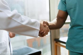 A doctor in a white coat and a nurse in teal scrubs shake hands. Image credit: ©master1305 – stock.adobe.com