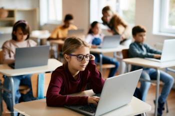 A child wearing glasses sits in a classroom among her peers who do not have glasses. Image credit: ©Drazen – stock.adobe.com