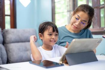 A woman with glasses helps a child, who may be her daughter, use a tablet. Concept image for online school, homeschool, screen time, myopia, and paediatric astigmatism. Image credit: ©K2L Family – stock.adobe.com