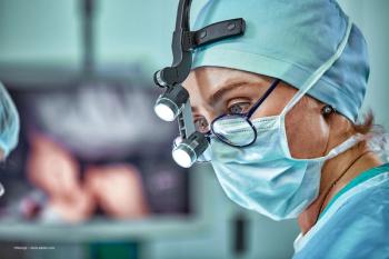 An eye surgeon with glasses stands masked in the operating theater. Image credit: ©Georgii – stock.adobe.com
