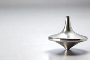 A silver spinning top sits on a flat, white surface. Image credit: ©suchetpong – stock.adobe.com – generated with AI