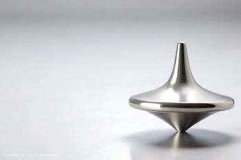 A silver spinning top sits on a flat, white surface. Image credit: ©suchetpong – stock.adobe.com – generated with AI