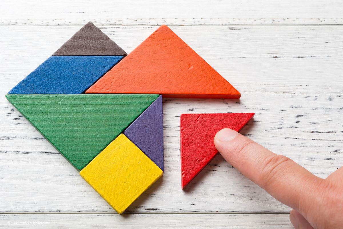A hand pushes a triangle-shaped tangram block into a colorful collection of other triangle blocks, all in various sizes. Image credit: ©Freer – stock.adobe.com
