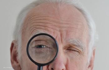 An elderly man holds a magnifying glass close to his eye. Image credit: ©Irina – stock.adobe.com